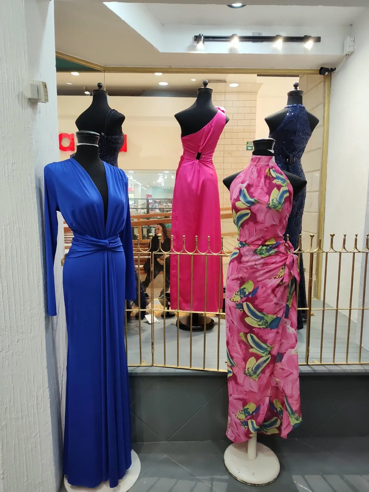 Tres vestidos largos en maniquí: azul rey de manga larga, fucsia de un hombro y estampado tropical