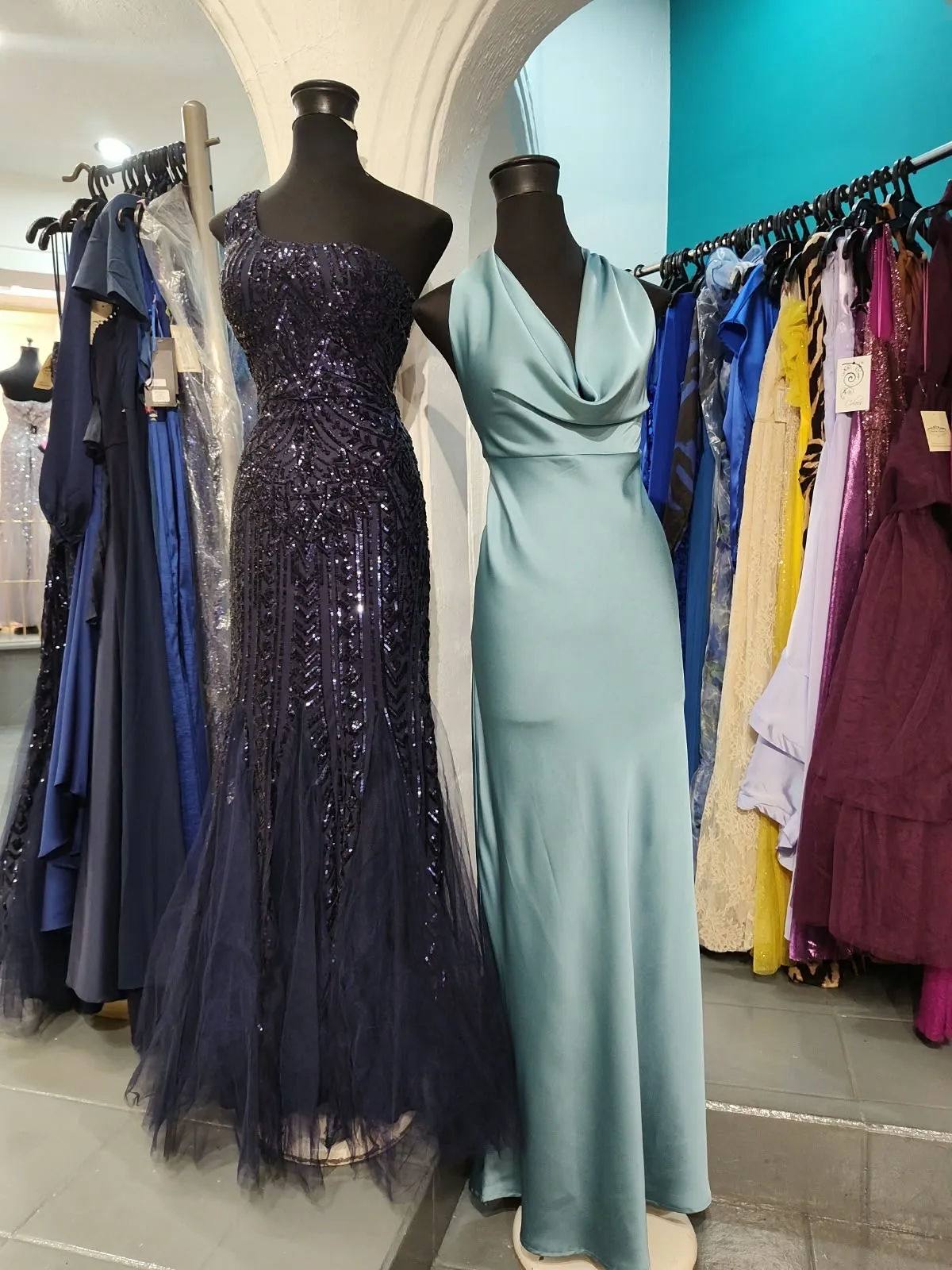 Vestido azul marino de lentejuela y vestido de satín aqua junto a un perchero de vestidos