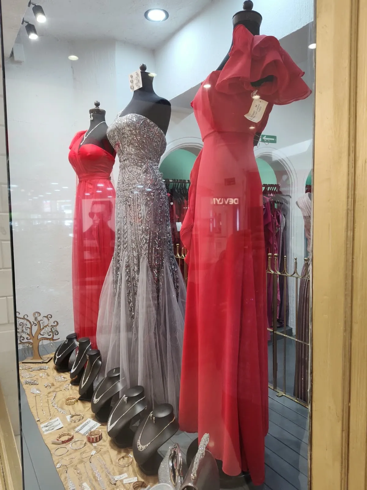Aparador con vestidos rojos y un vestido plateado de brillo, con joyería al frente