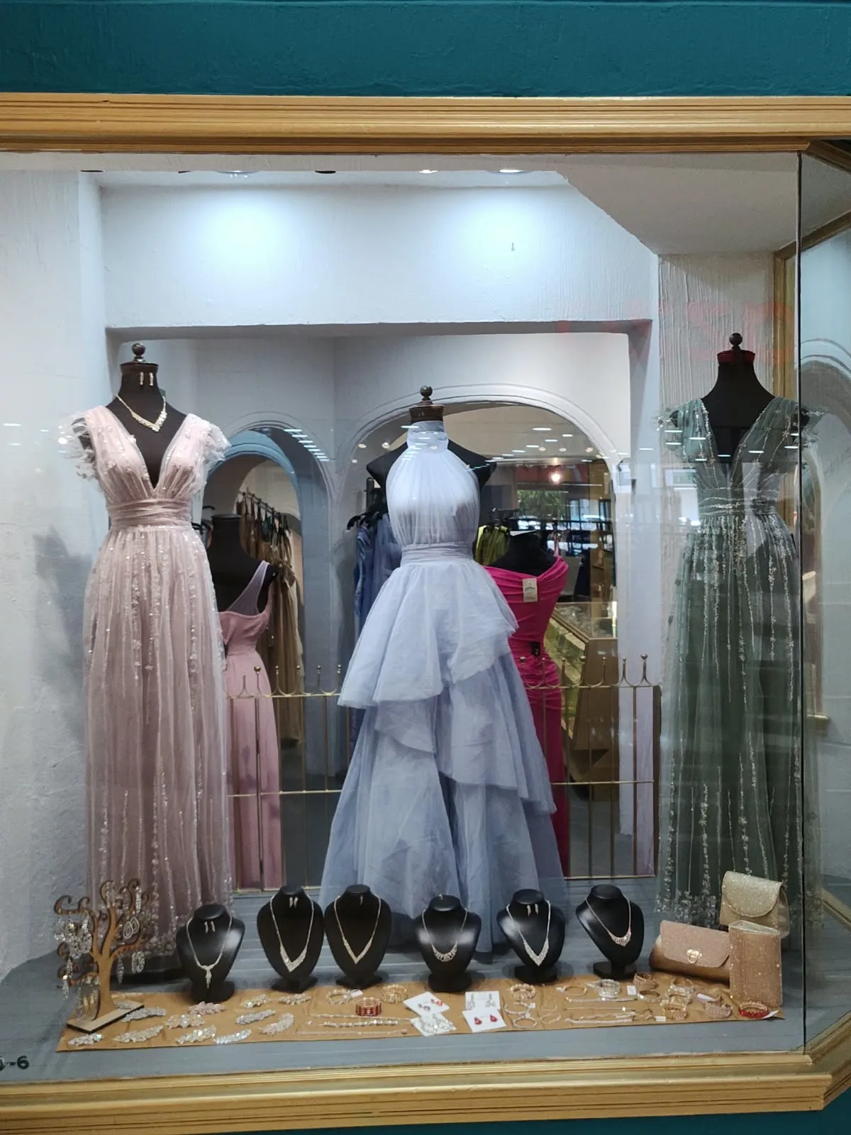 Aparador con vestidos rosa, lavanda de holanes y verde salvia, con collares al frente